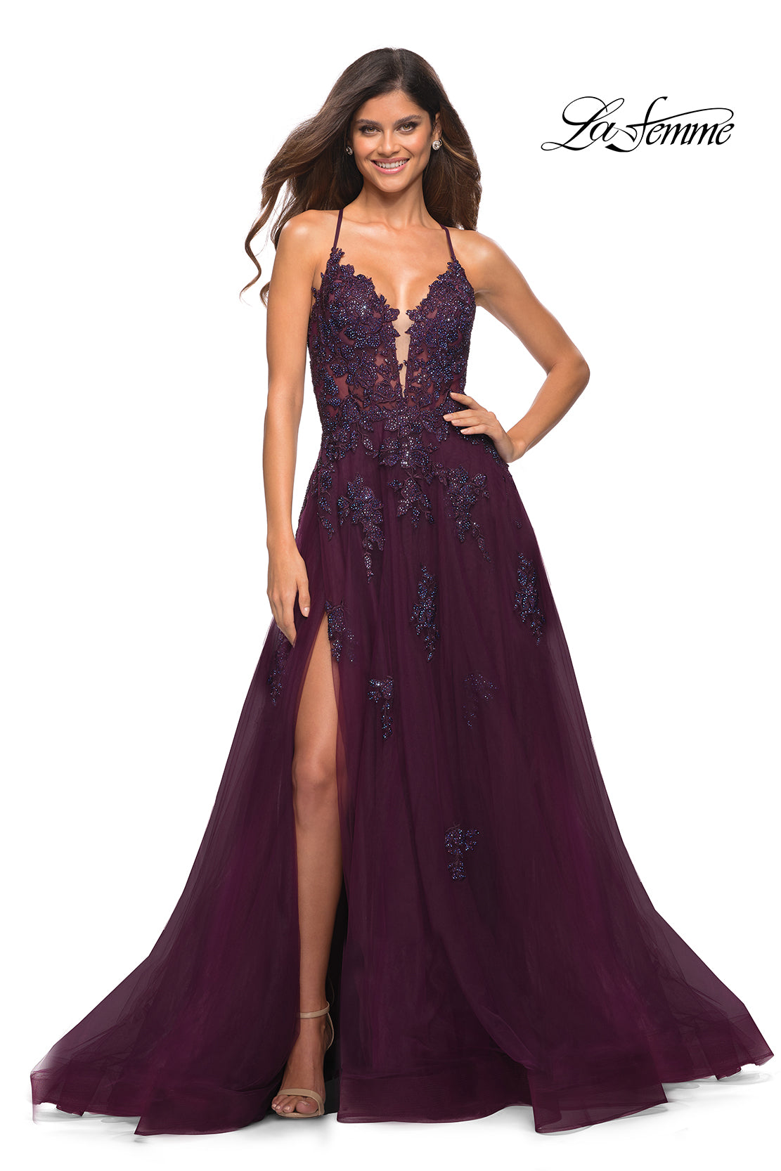 A woman smiles in a La Femme Open-Back Long Ball Gown with lace, deep purple and floor-length, featuring a plunging neckline and high leg slit. The La Femme logo appears in the corner.